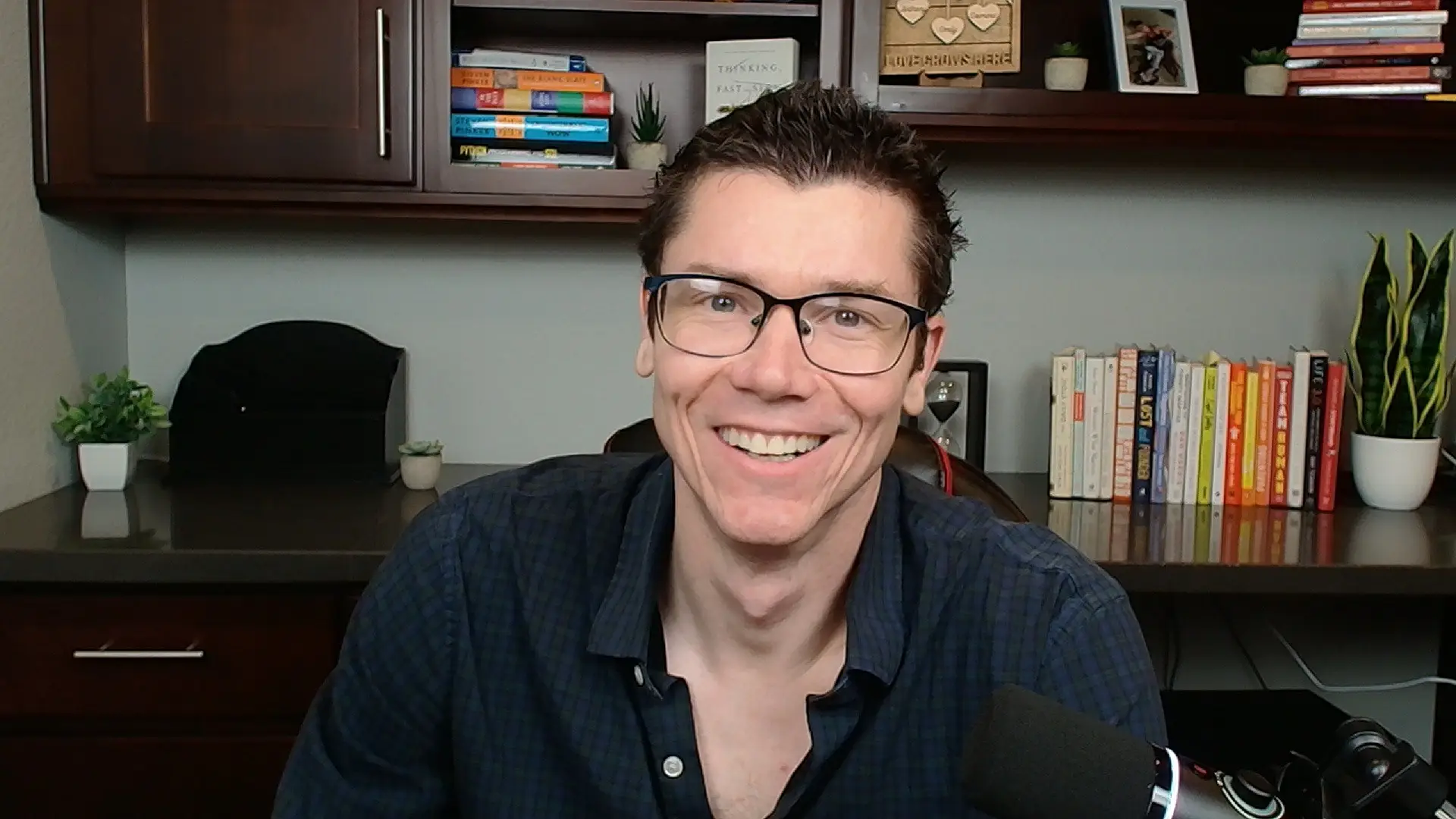 TJ Robertson at his home office desk, in front of a wall cabinet and two shelves of books.